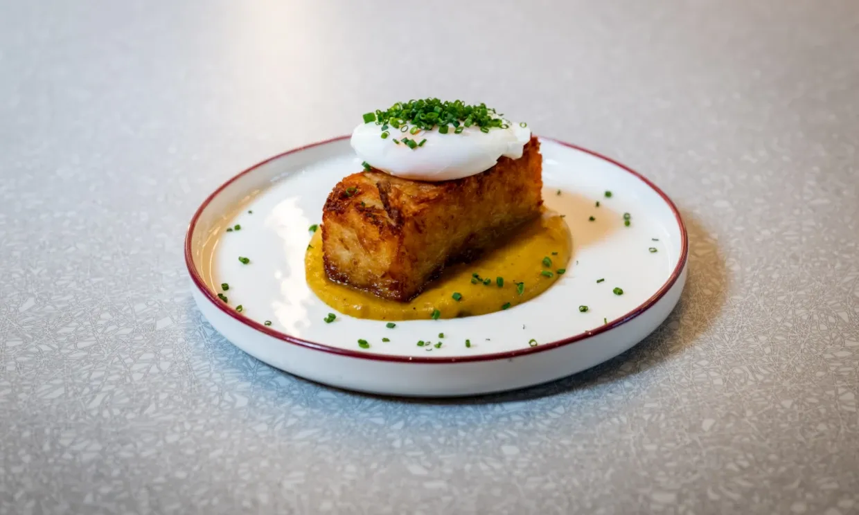 A large hash brown sits on curry sauce and is topped by an egg with garnish. 