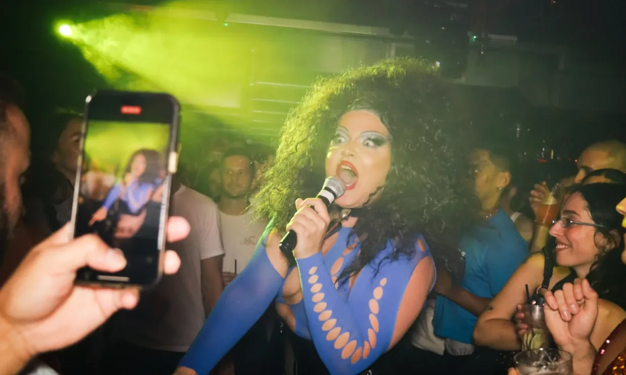 A drag performer in a crowd sings on a microphone.