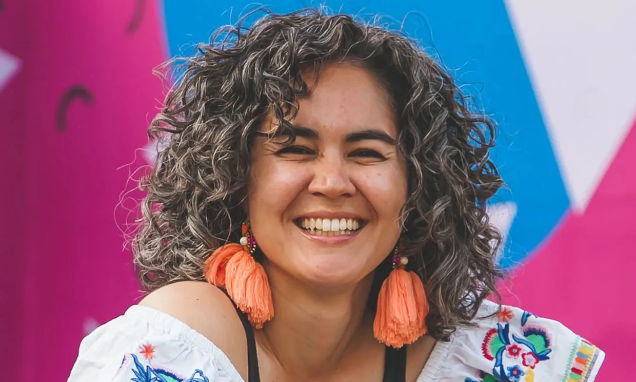 Photo of the artist smiling, a woman with curly hair and large orange earrings.