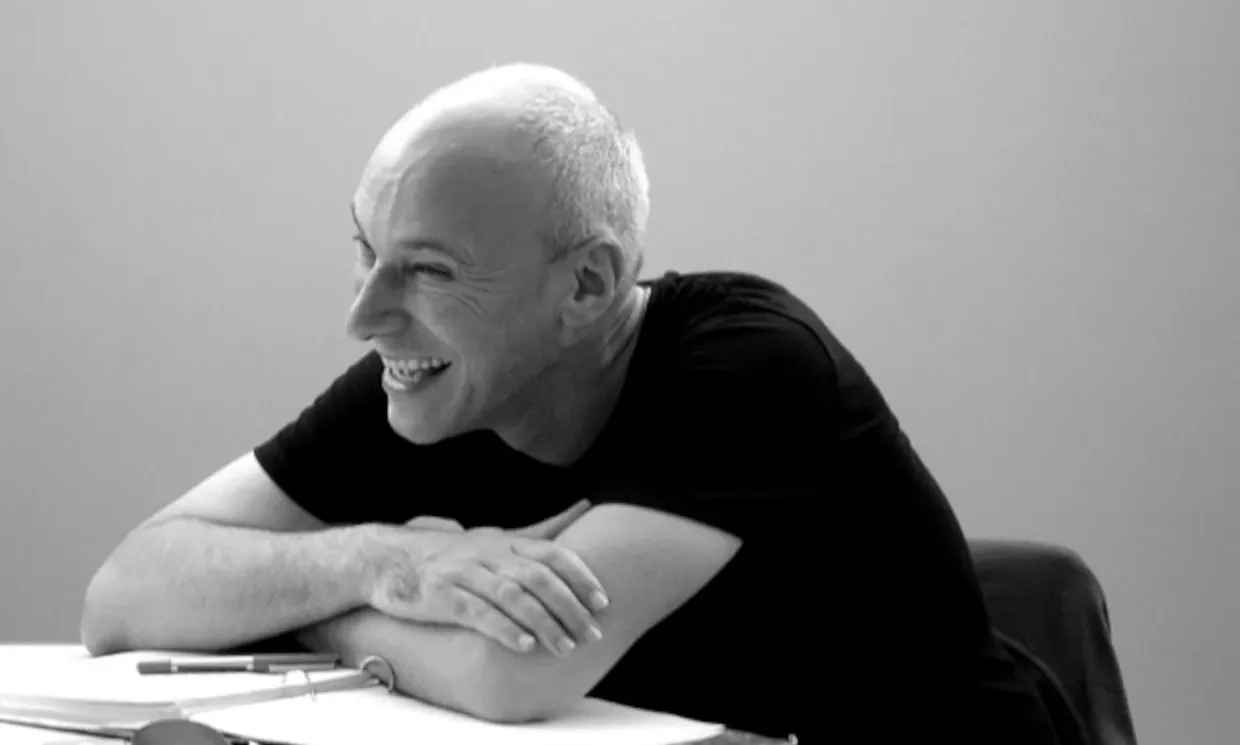 Black and white photo of Tony Graham, laughing while sat at a desk. 