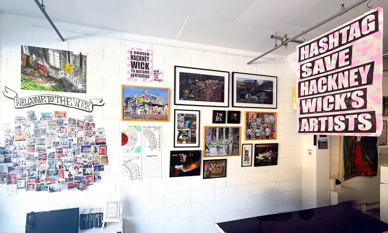 More art and photos on the wall. A big sign saying HASTAG SAVE HACKNEY WICK'S ARTISTS is hanging nearby.