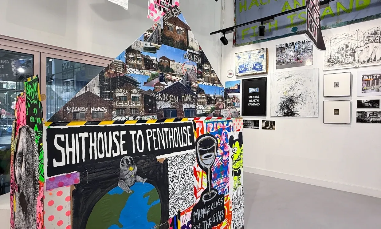 An installation in the shape of a house. It says SHITHOUSE TO PENTHOUSE and is made out of collaged paper and graphics