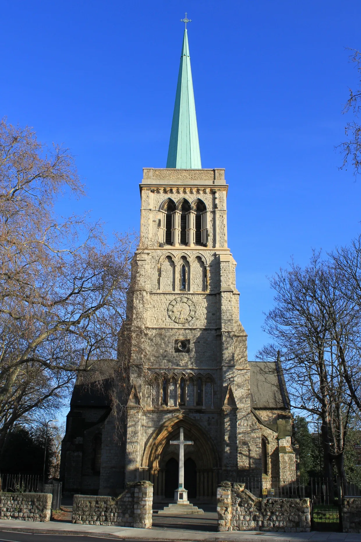 The outside of the church. In front is a cross sculpture and a large steeple