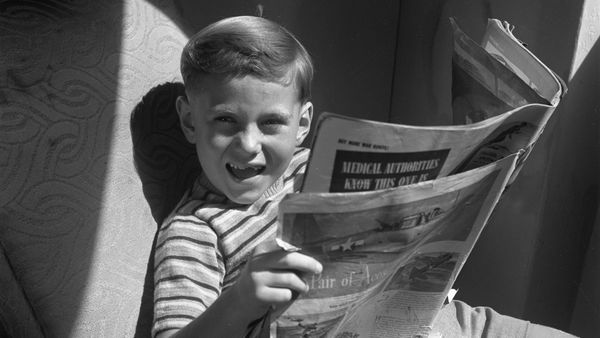 A young boy reads a newspaper. 
