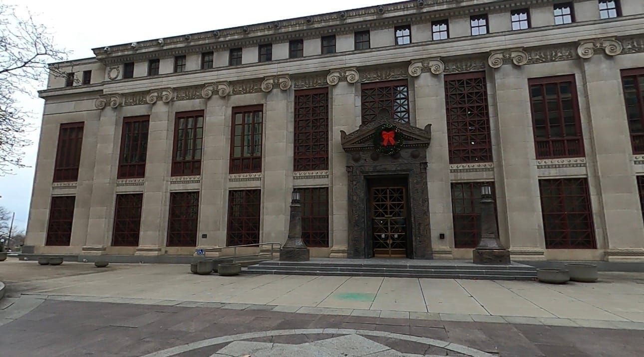 A three story building with open plaza and a few steps leading to a decorative door with a holiday wreath hung over the door