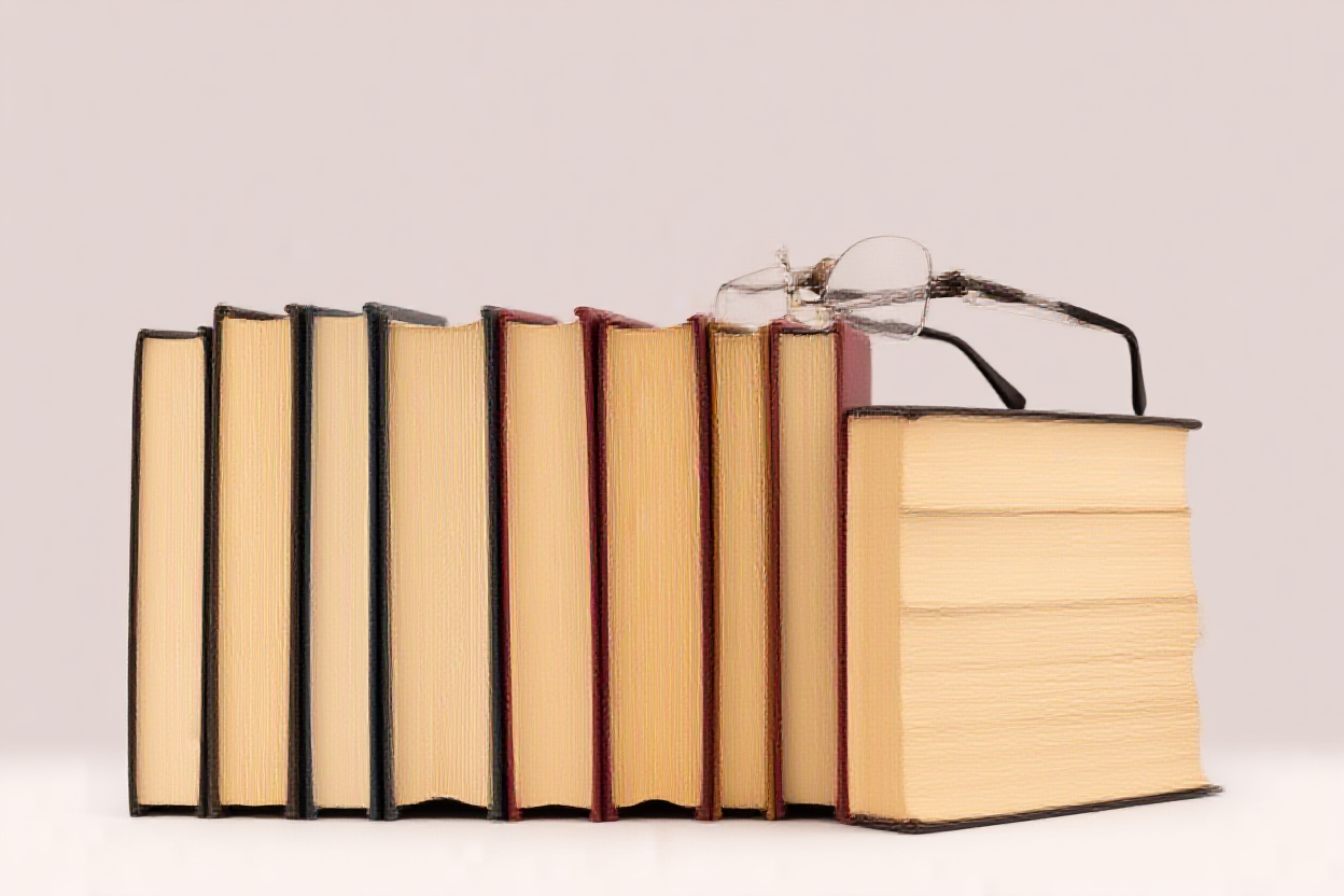 Ein Stapel bunter Hardcover-Bücher, die ordentlich auf einem Regal neben einer Les Brille angeordnet sind