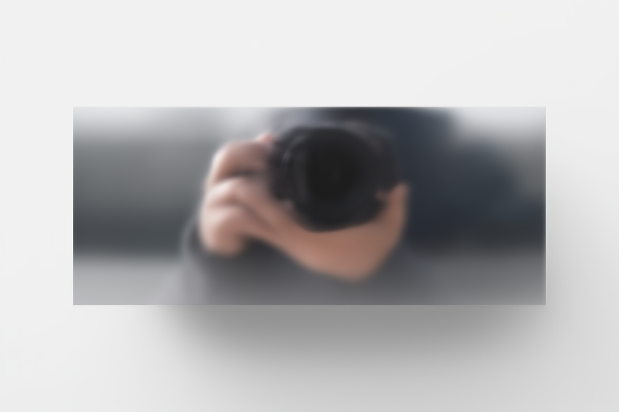 Ein Fotograf hält eine Kamera mit beiden Händen und nimmt in einer städtischen Umgebung ein Bild auf, wobei verschwommene Stadtgebäude im Hintergrund zu sehen sind.