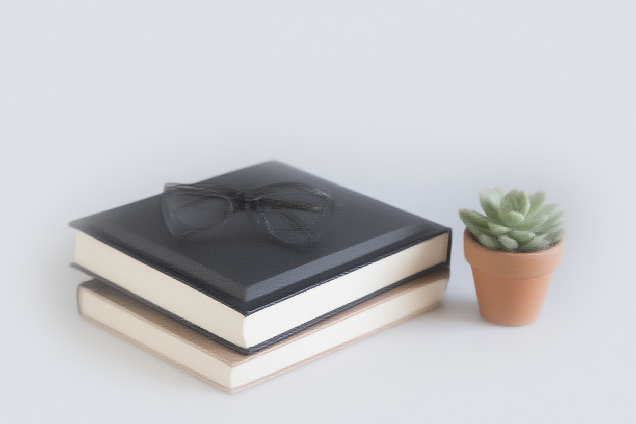 Ein Stapel Hardcover-Bücher mit einem Paar Lesegläsern darauf, neben einer kleinen Sukkulentenpflanze in einem te