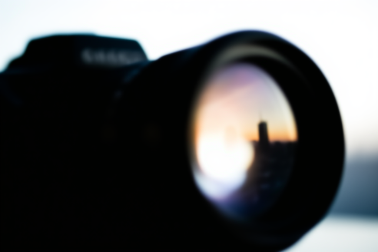 un gros plan sur l'objectif d'un appareil photo numérique reflétant un skyline urbain avec une douce lumière du matin