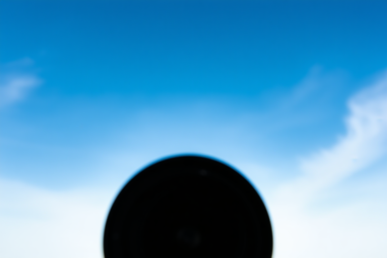eine Profikamera-Linse zeigt auf einen hellblauen Himmel mit zarten Wolken