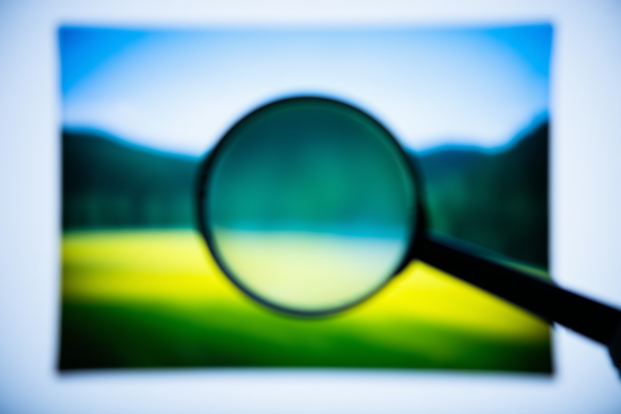 eine Lupe, die ein gedrucktes Foto auf Details untersucht, weiches Tageslicht, breites Landschaftsfoto