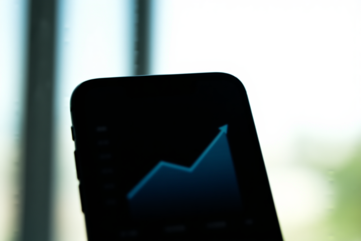 eine Nahaufnahme eines Smartphone-Bildschirms, der einen Verkaufsgraphen mit einer aufwärts gerichteten Trendlinie auf einem unscharfen Bürohintergrund anzeigt, weiches d