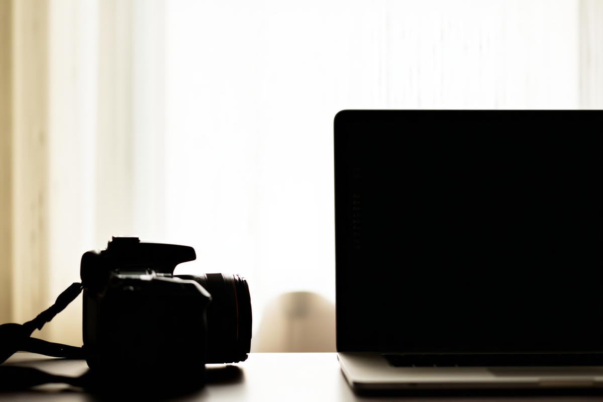 A professional photographer reviewing metadata tags on a laptop screen next to a digital camera lens, soft natural light, wide landscape shot