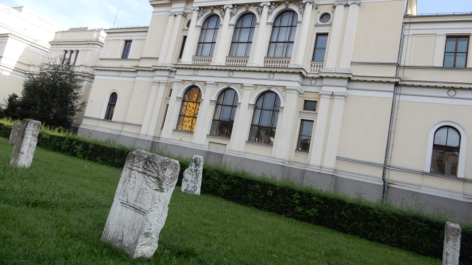 Små stećci foran Nationalmuseet i Sarajevo. Det ikoniske Holiday Inn-hotel spejles i museets vindue. Herfra blev Suada Dilberović og Olga Sučić snigmyrdet under etnisk blandede antikrigsprotester den 5. april 1992. (Jimmy Munk Larsen)