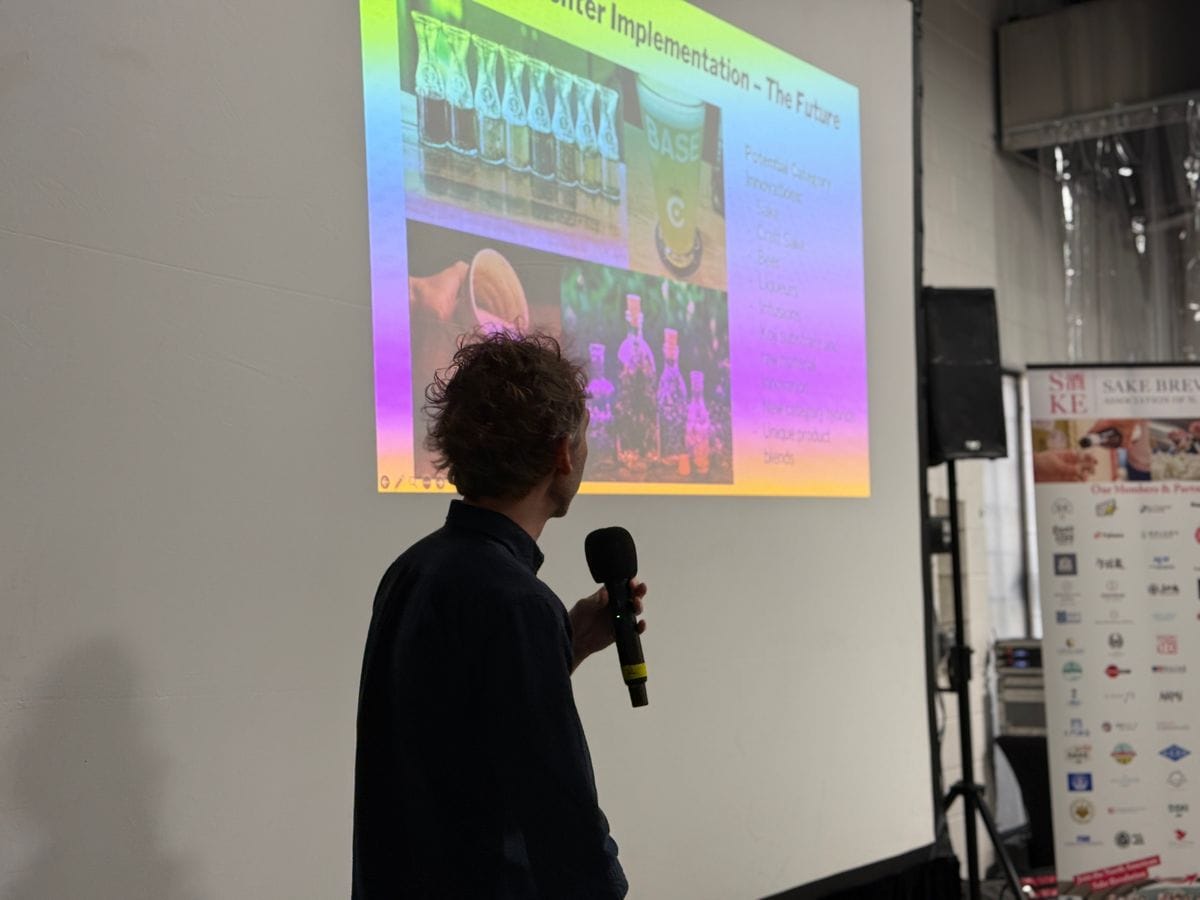 A presenter discussing sake fermentation beside a projected slide during Industry Day.
