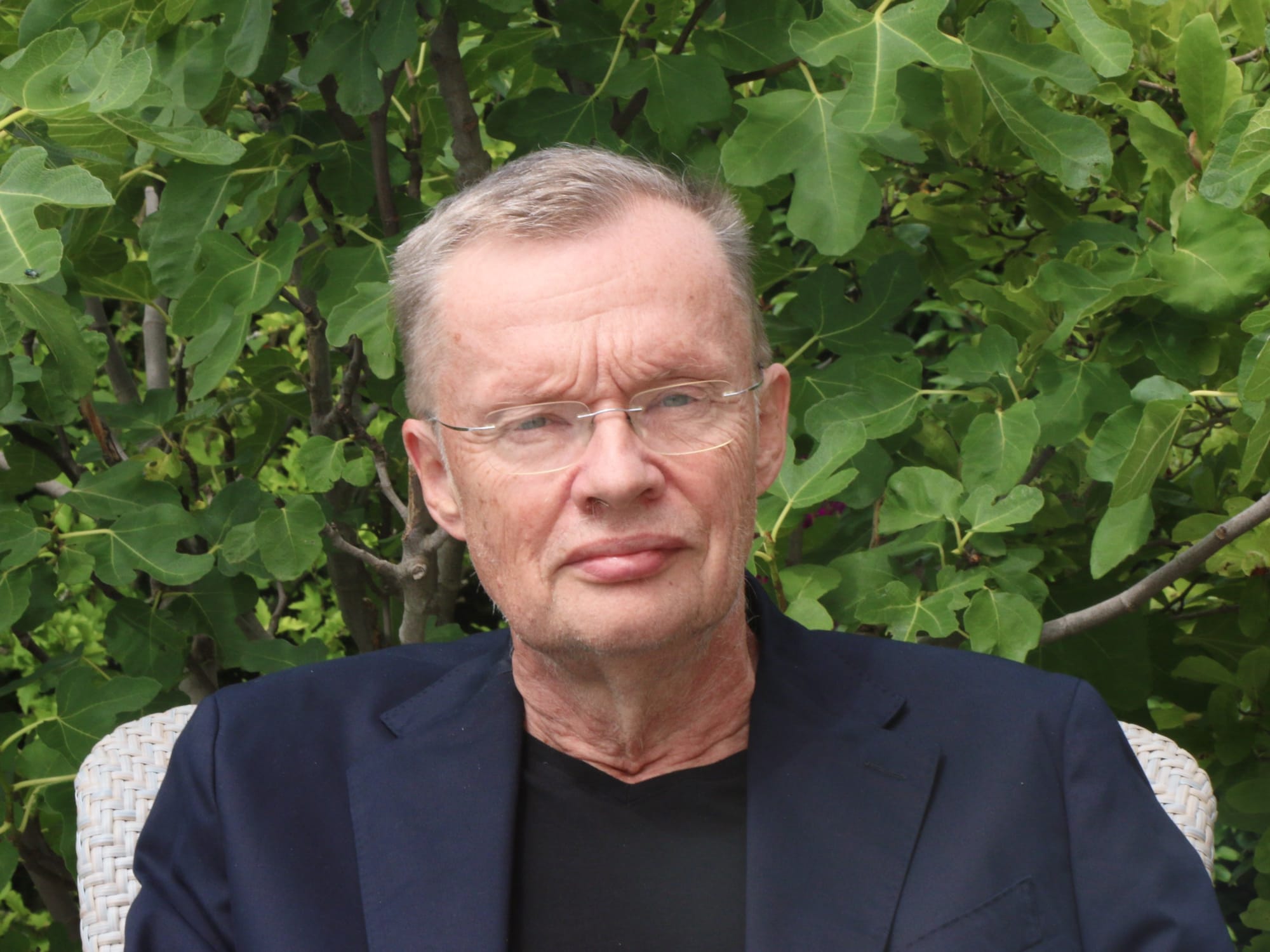 Porträt des Historikers Volker Reinhardt. Er sitzt auf einem Stuhl im Garten.