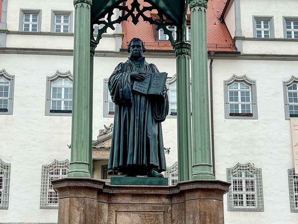 Denkmal von Martin Luther. Luther trägt einen Umhang und hält ein geöffnetes Buch in der Hand.