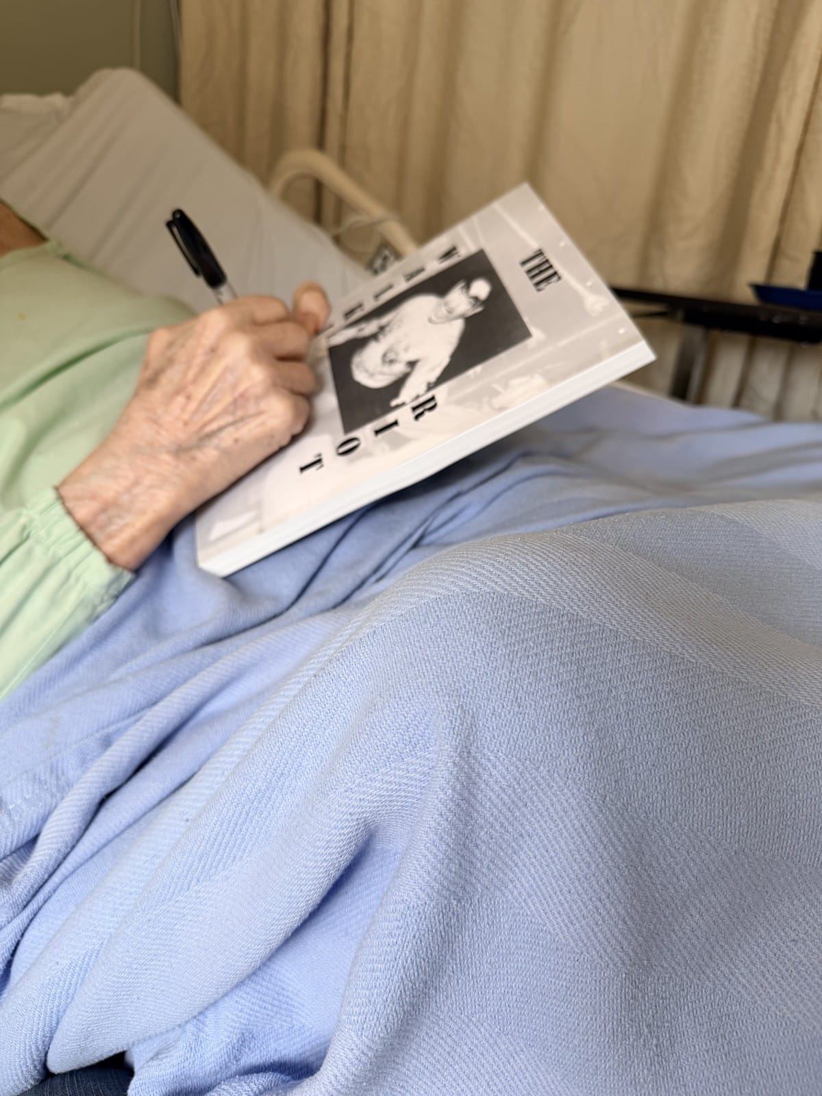 Flying Fred Curry's aged hand signing The Walking Riot — the book he wrote about his father Wild Bull Curry — from his hospice bed, April 2026.