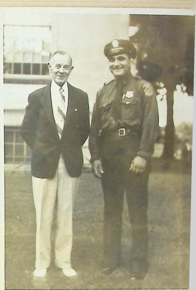 A young officer Bull Curry beaming in uniform beside an older man in a blazer on a lawn