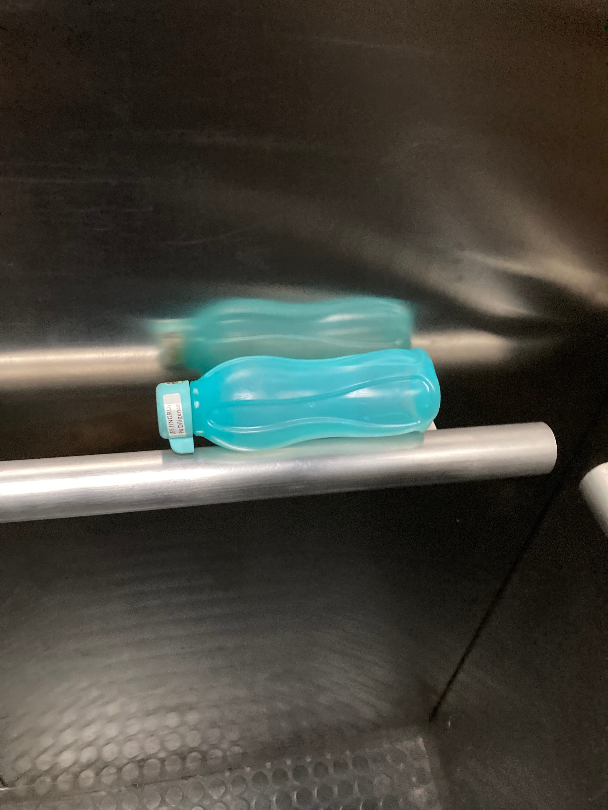 A turquoise water bottle lays on its side on a handrail in an elevator