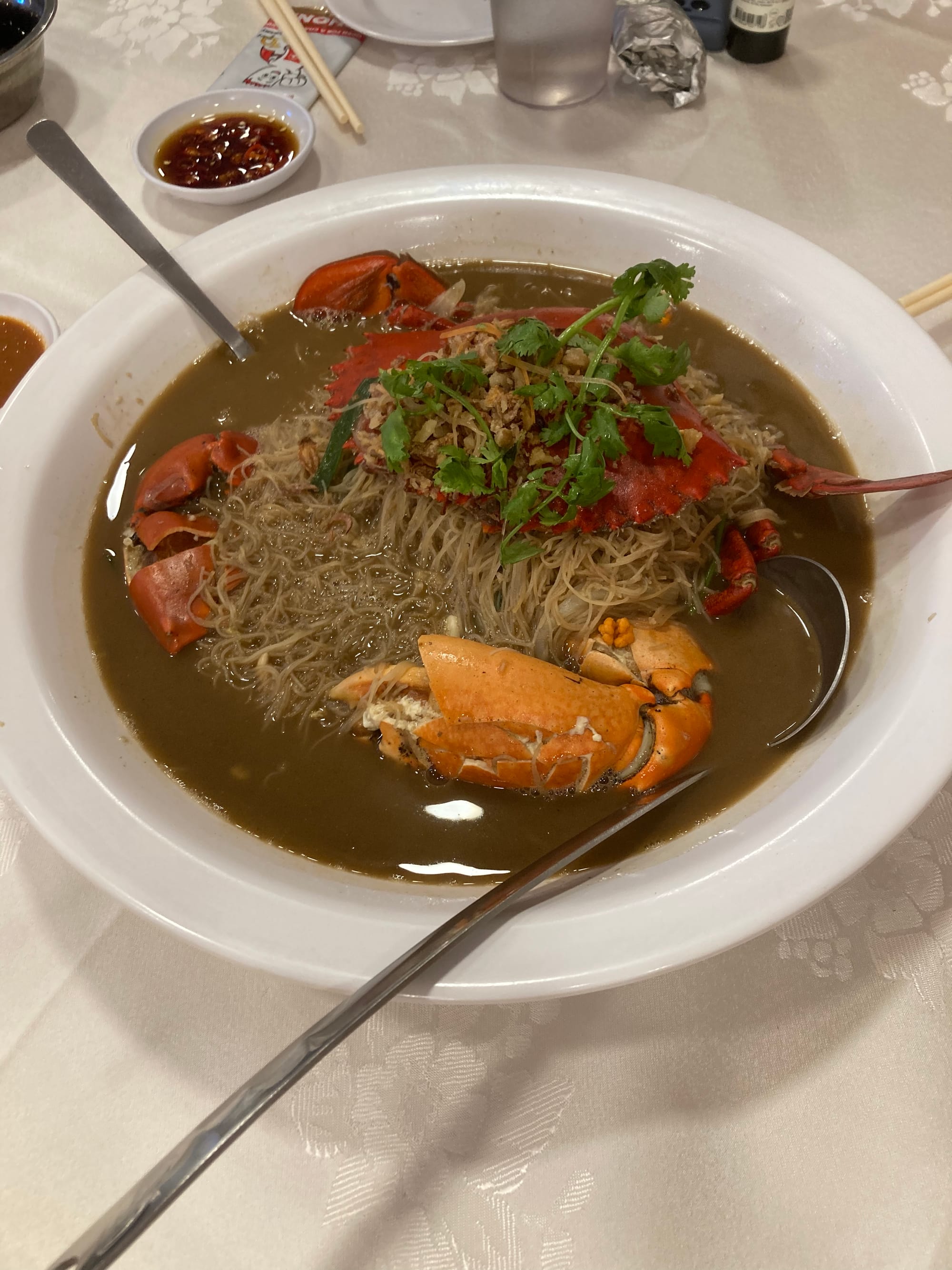 A large white dish of crab and vermicelli in a dark broth
