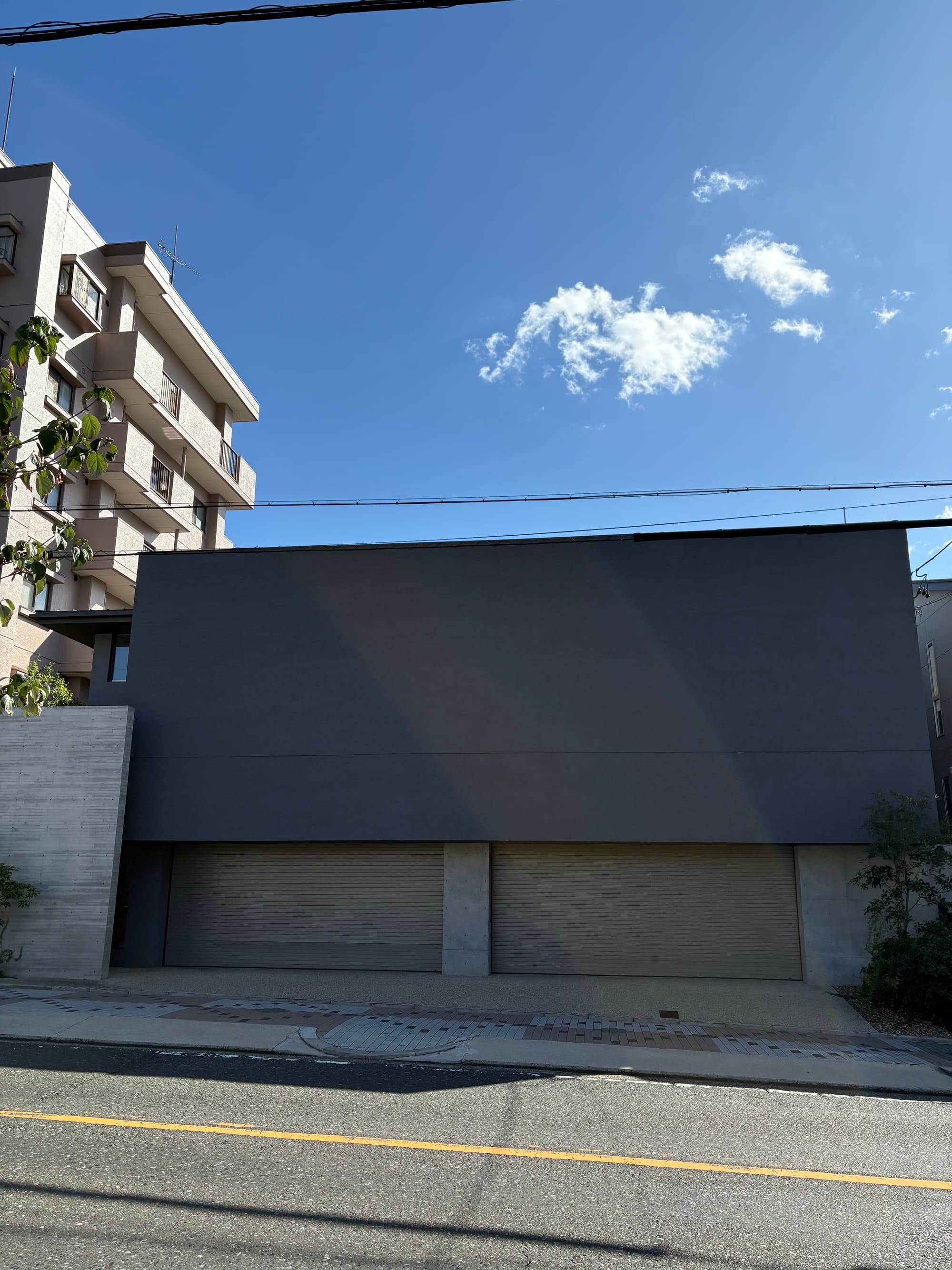 A boxy house in grey with no windows at all and two garages shuttered by a metal door.