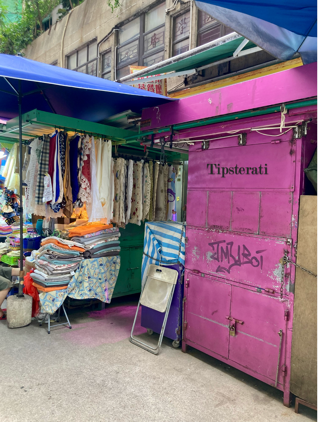 A shuttered street stall (in purple) stands next to another selling towels and blankets.
