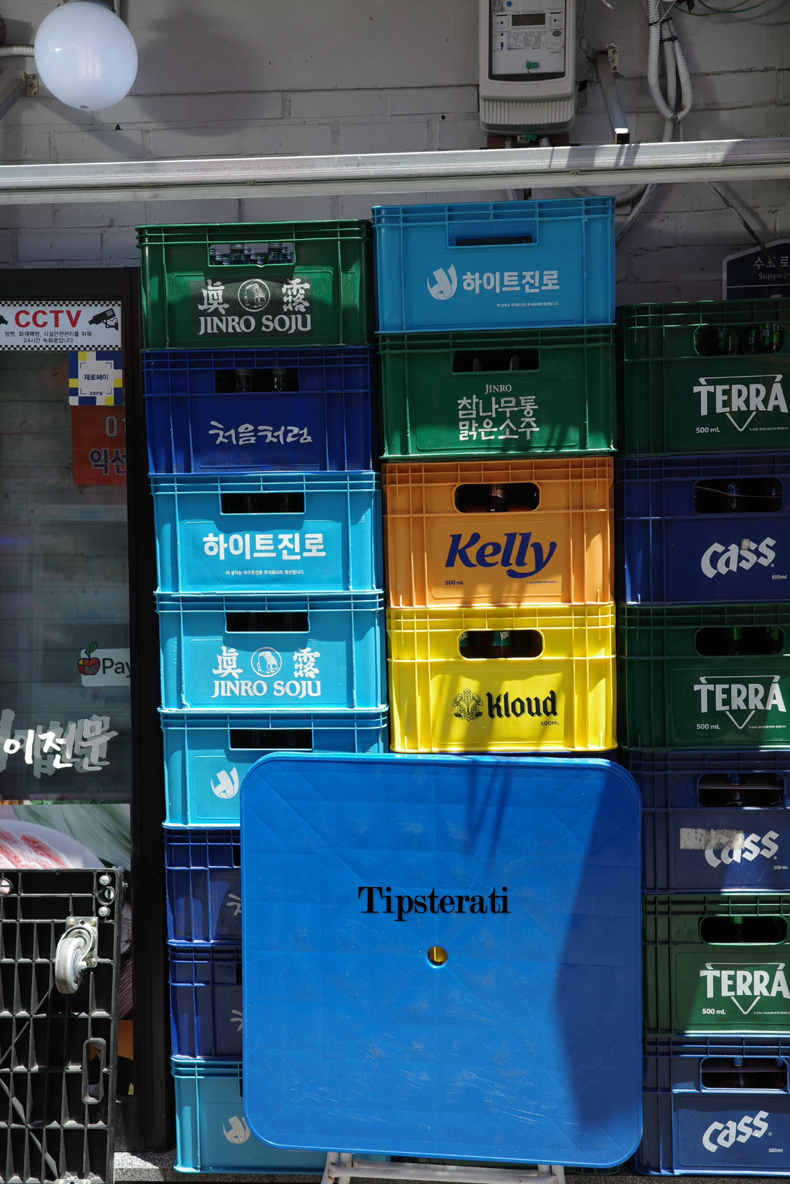 A blue foldable table stands in front of stacks of colourful beer and soju crates.