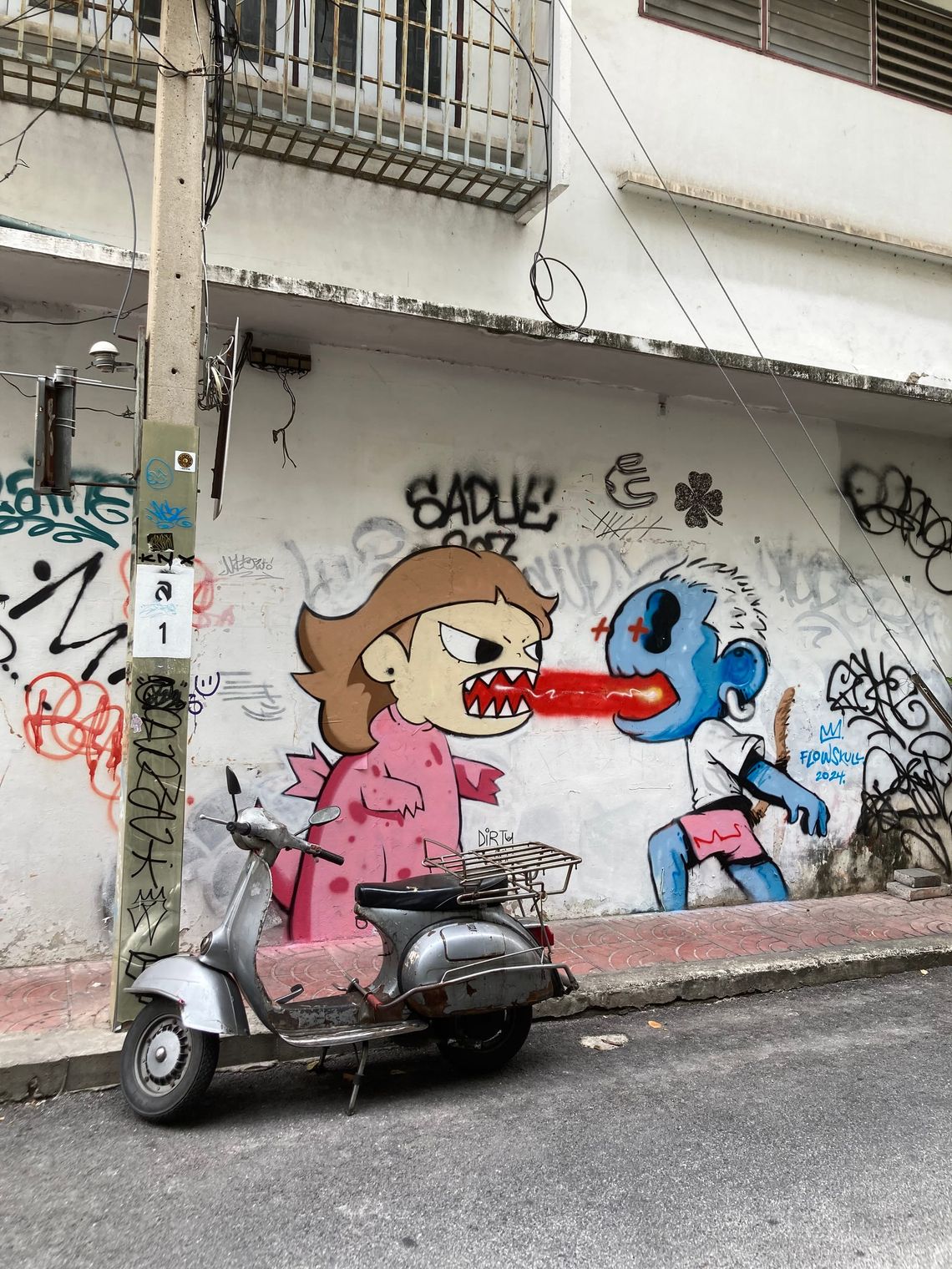 A grey moped is parked in front of graffitied wall.