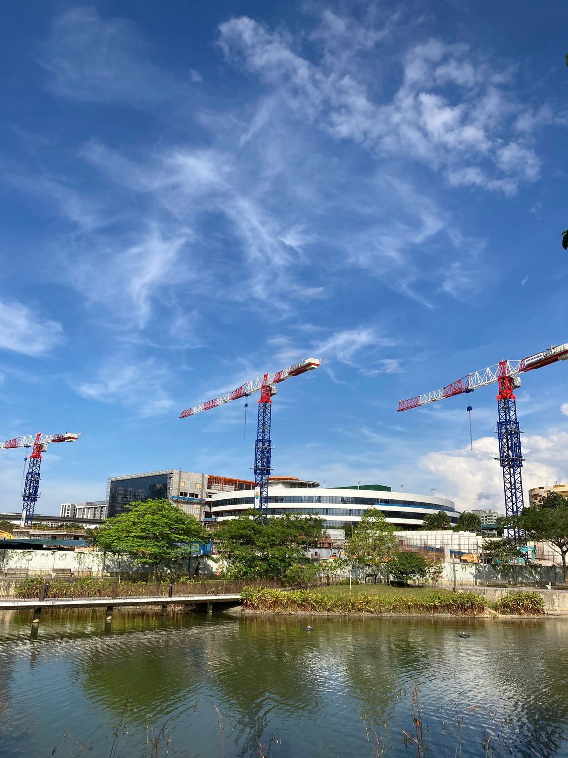 Three construction cranes stand tall against a blue sky