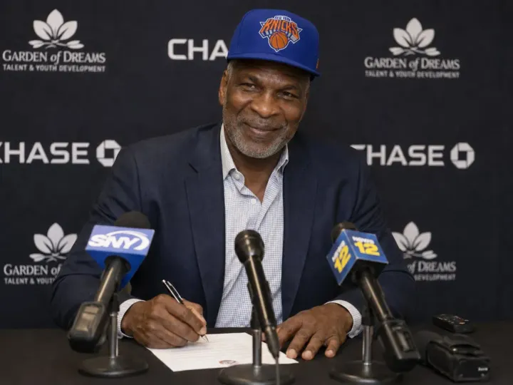 Picture of modern-day Charles Oakley signing a contract with a Knicks hat on.