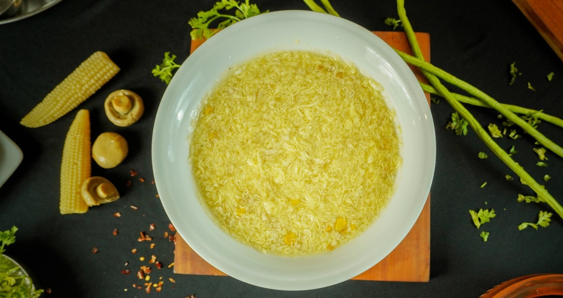 A bowl of creamy yellow corn soup and fresh vegetables.
