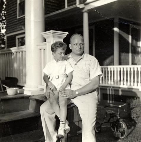 Richard Roth Jr sits on the lap of Richard Roth Sr in a front yard