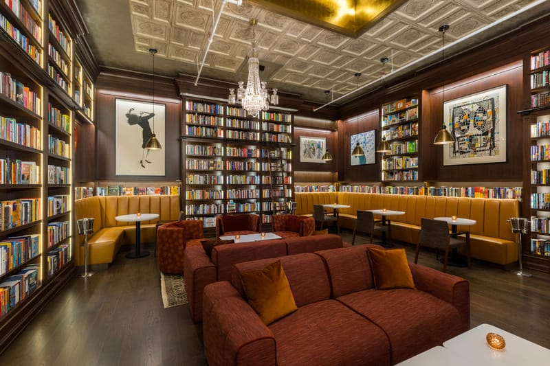 Photo of Bibliotheque bookstore bar in Manhattan, couches and tables sit in front of dark wood bookcases interrupted by large paintings