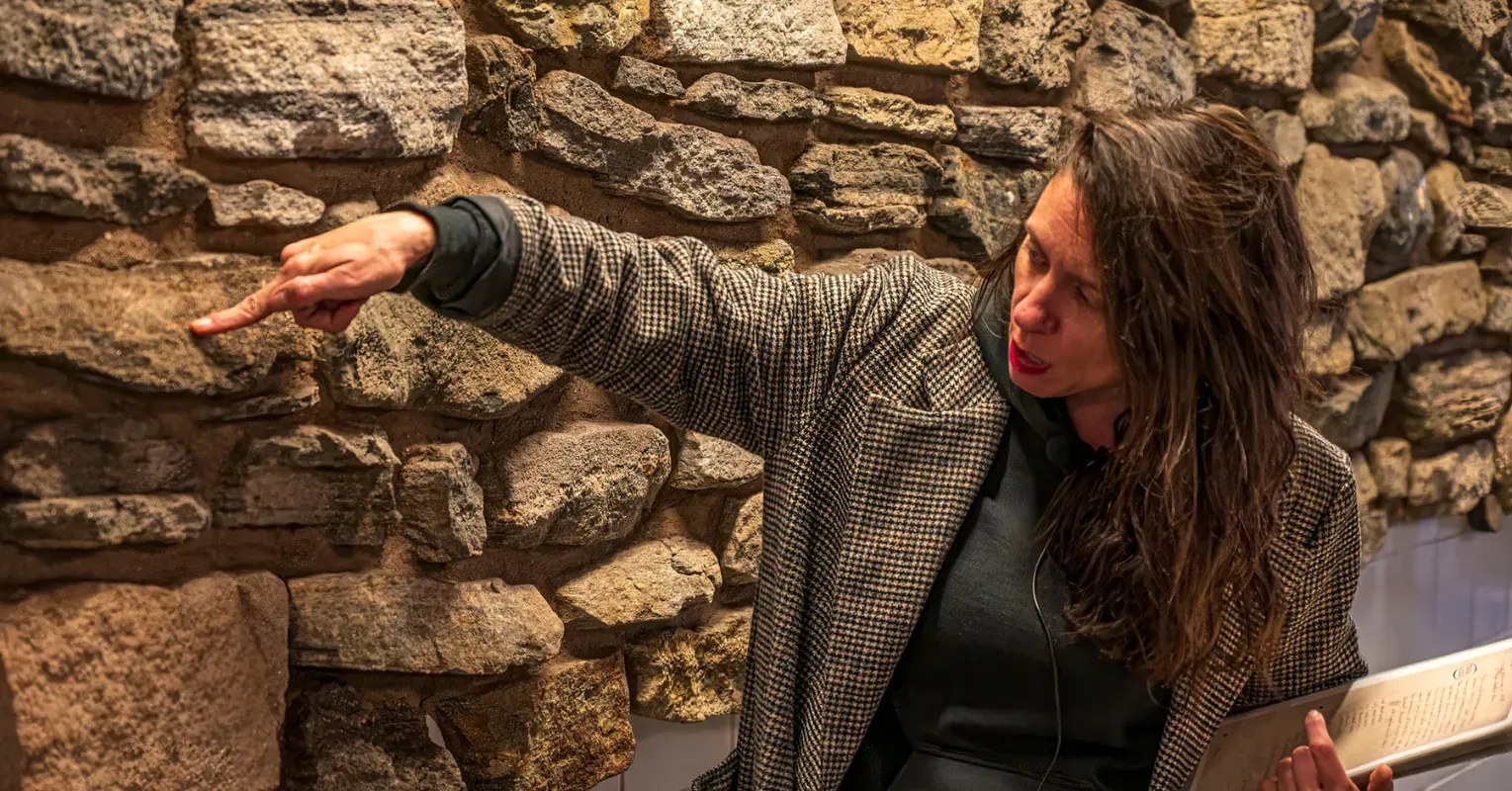 A woman point to a piece of a stone wall