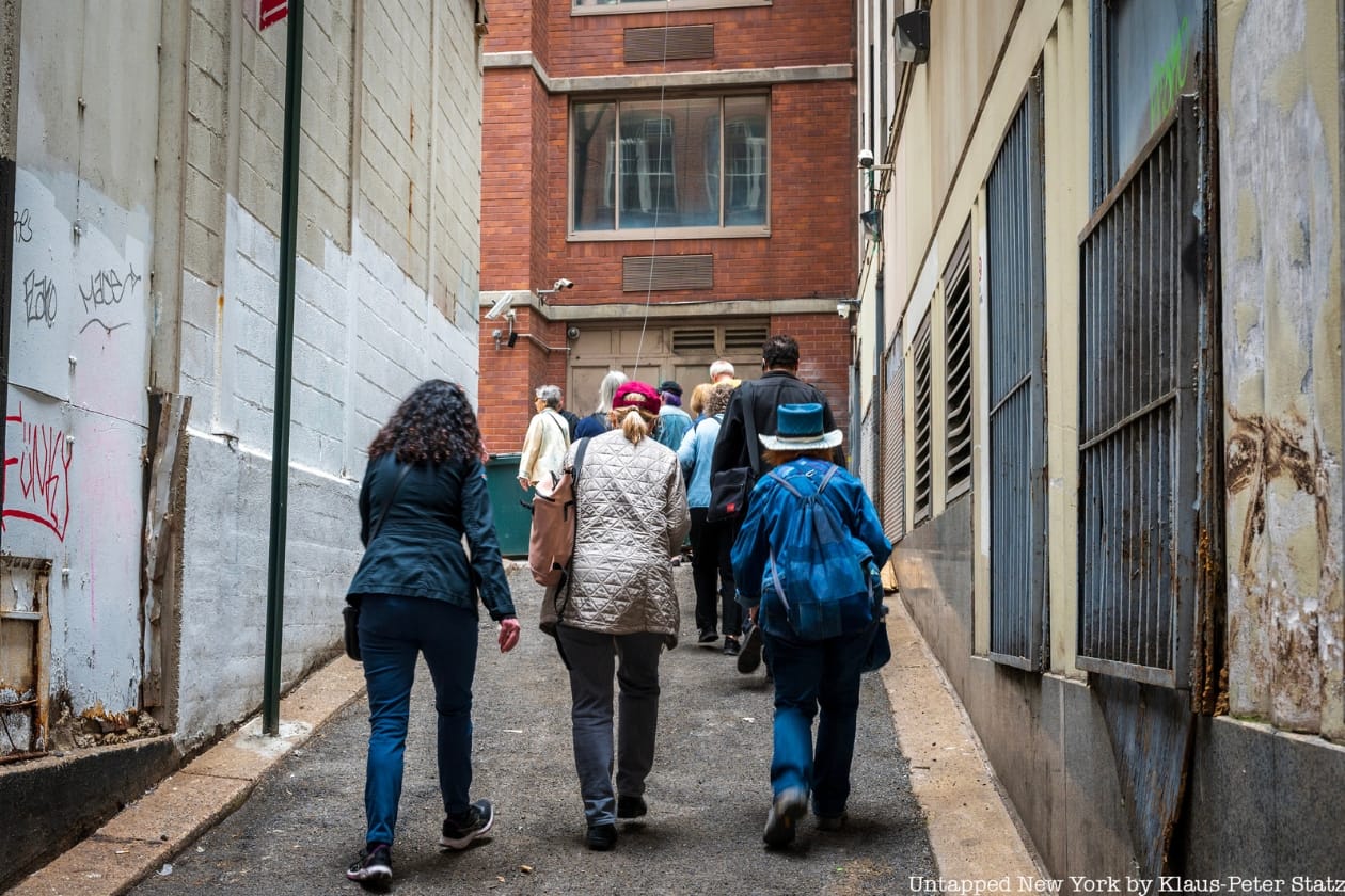 NYC Spies of the American Revolution tour group climb Golden Hill, walking up a street in an alley
