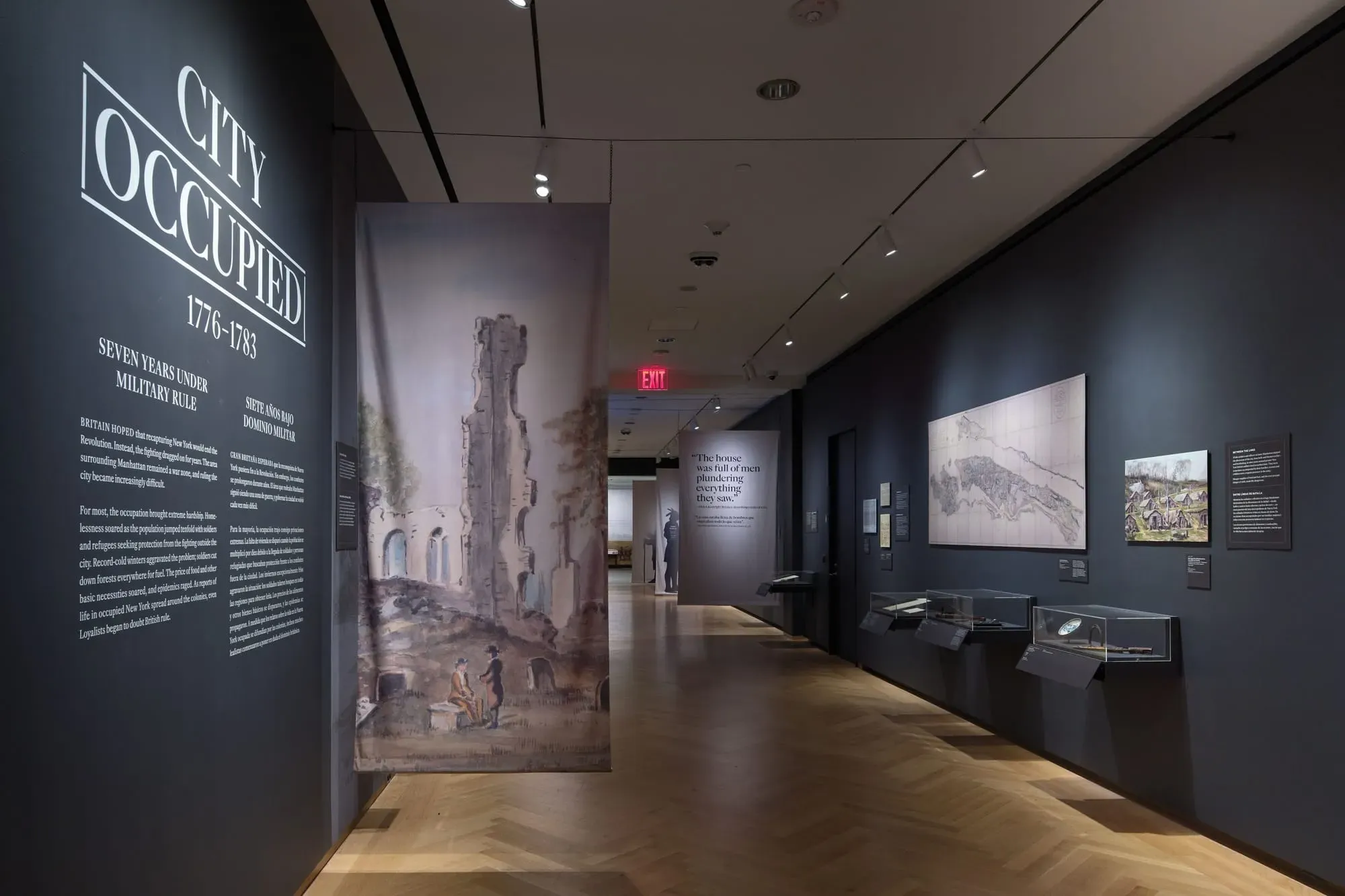 Gallery view of the "City Occupied, 1776–1783: Seven Years Under Military Rule" section of The Occupied City exhibit, featuring a large painted ruin, historical maps, artifacts in glass cases, and the quote "The house was full of men plundering everything they saw."