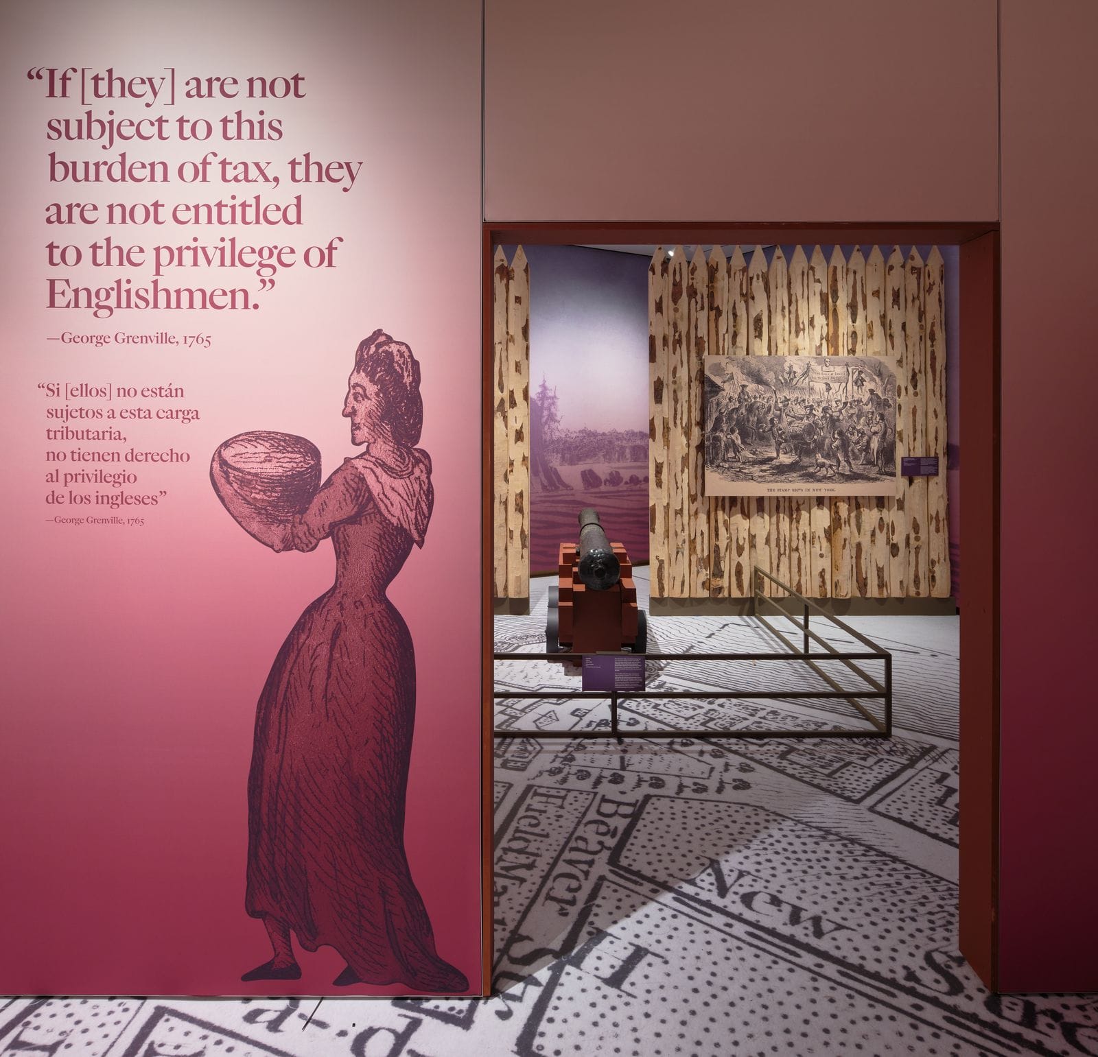 A room in The Occupied City exhibit with a large-scale quote by George Grenville (1765) on a deep red wall alongside a period illustration of a woman, opening into a gallery featuring a cannon, a printed floor map of colonial New York, and a historical engraving.