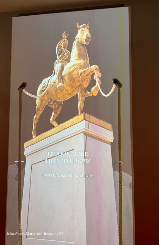An interactive digital installation showing the gilded equestrian statue of King George III at Bowling Green, with actual ropes visitors can pull to recreate its toppling. Text on screen reads "It Took More Than One Rope!"