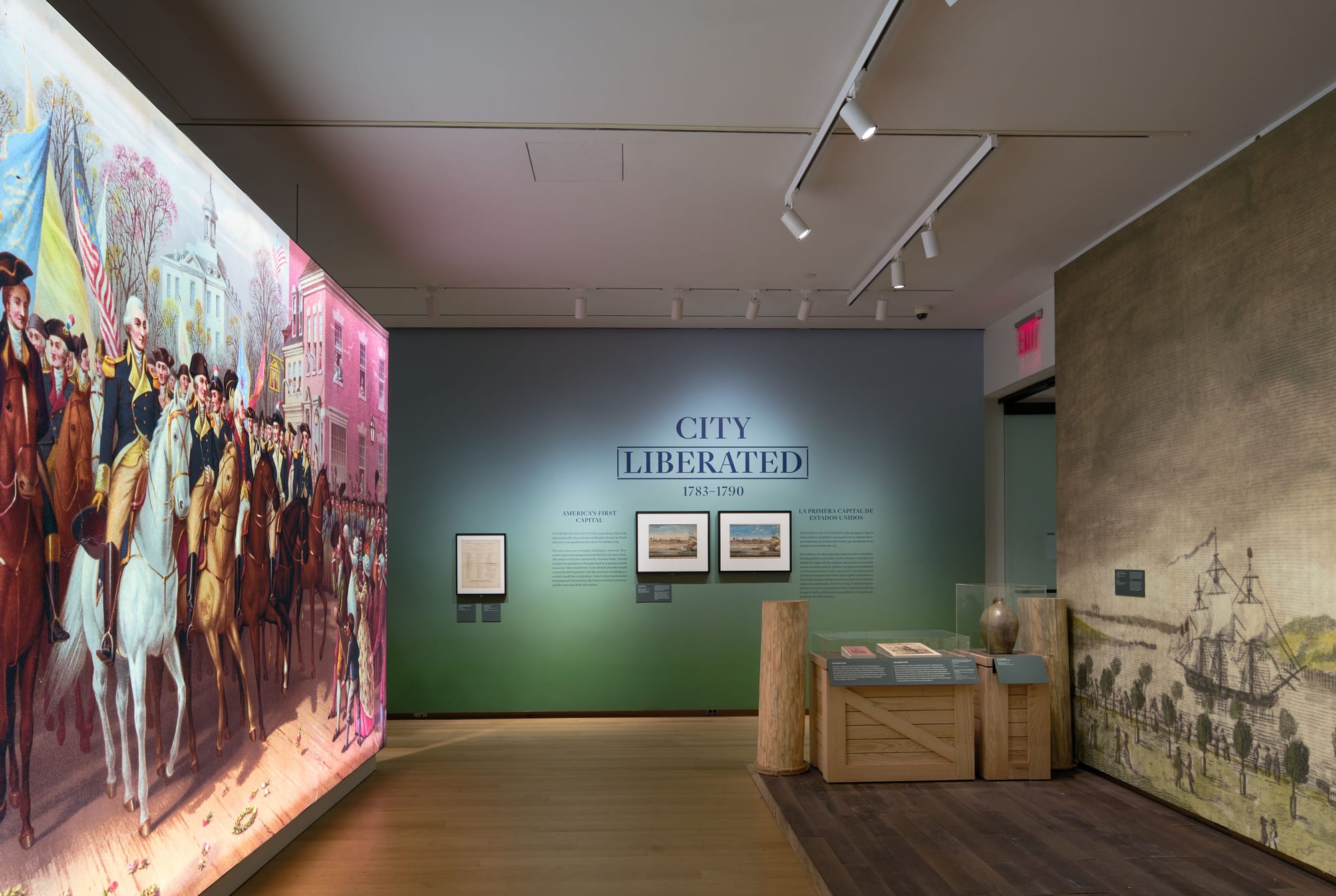 Gallery view of the "City Liberated, 1783–1790" section of The Occupied City exhibit at MCNY, featuring a large-scale reproduction of a painting showing George Washington's triumphal entry into New York, with framed historical prints and artifacts on display.