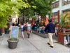 People walking on a sidewalk past a curbside dining set up