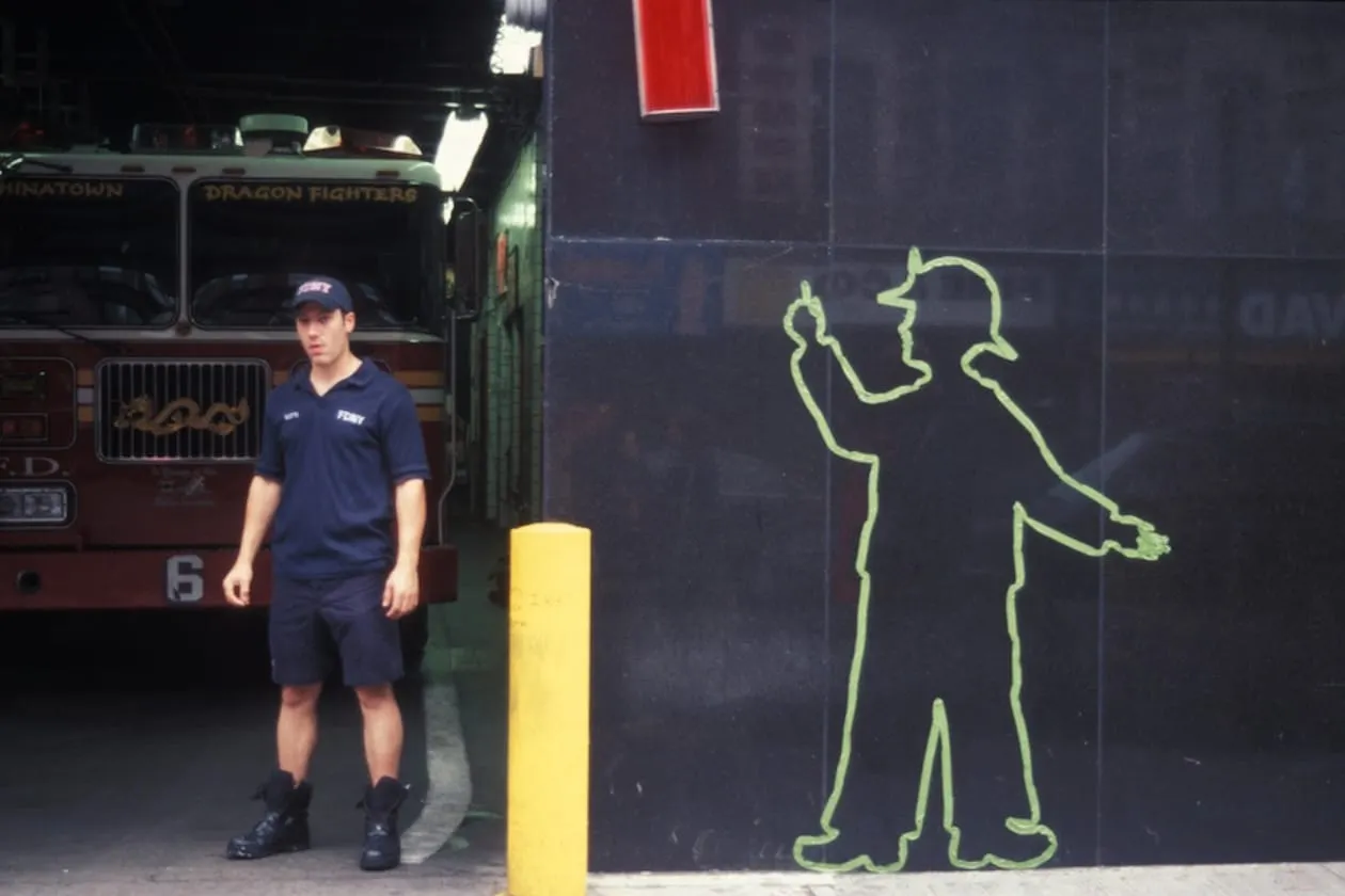 A firefighter stands beside a life-size tape silhouette outside a Manhattan firehouse.