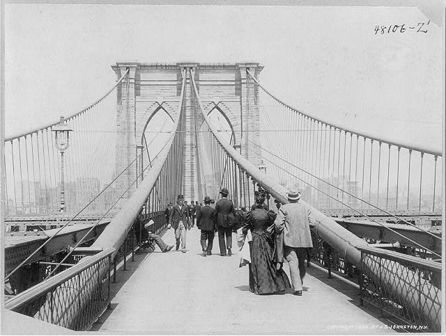Black and white photo of people walking across the Brooklyn Bridge