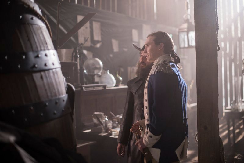 Two actors in Revolutionary War-era costume examine what appears to be the Turtle submarine in a candlelit workshop, in a scene from AMC's TURN: Washington's Spies.