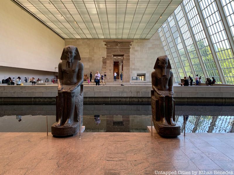 A front facing view of the Temple of Dendur with two Egyptian statues in the foreground.