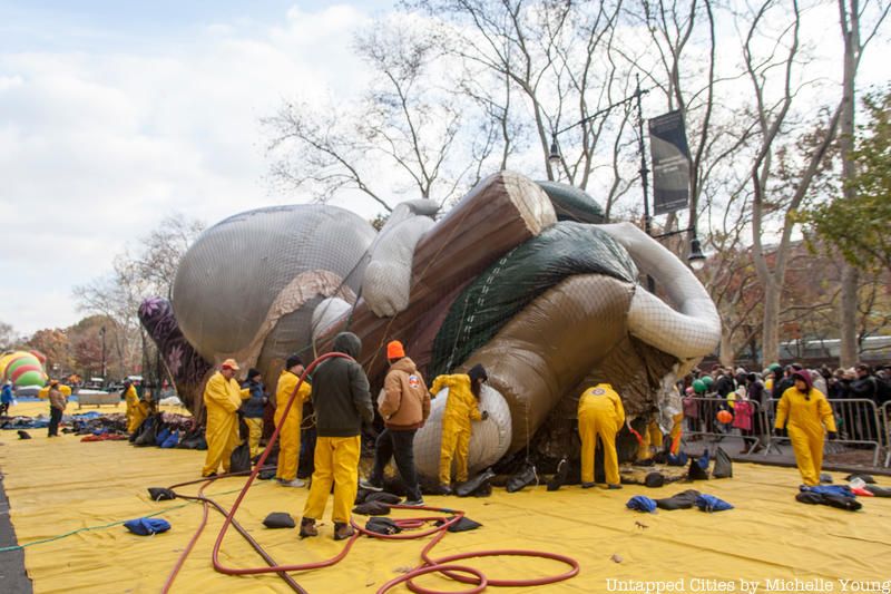 People in yellow jumpsuits gathering around a Macy's Thanksgiving Day parade balloon being inflated
