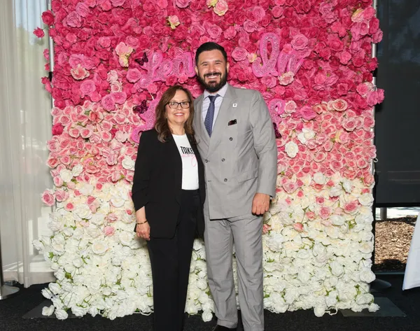Two attendees pose in front of a rose-covered photo wall at the 2025 Lean In Latinas Take Charge Conference.