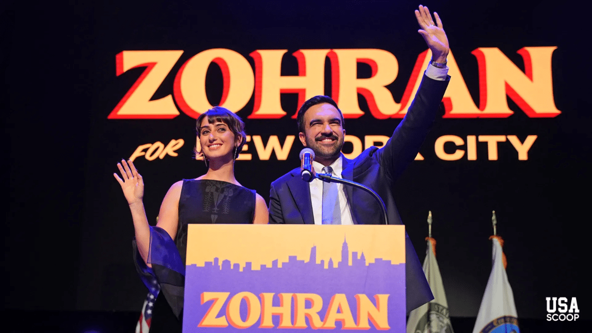 Zohran Mamdani and his wife Meher standing on stage waving to supporters after winning the New York City mayoral election