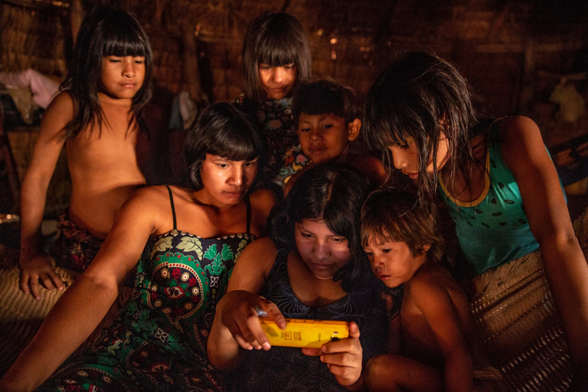 Um grupo de meninas e jovens indígenas contempla imagens em um telefone celular em sua aldeia