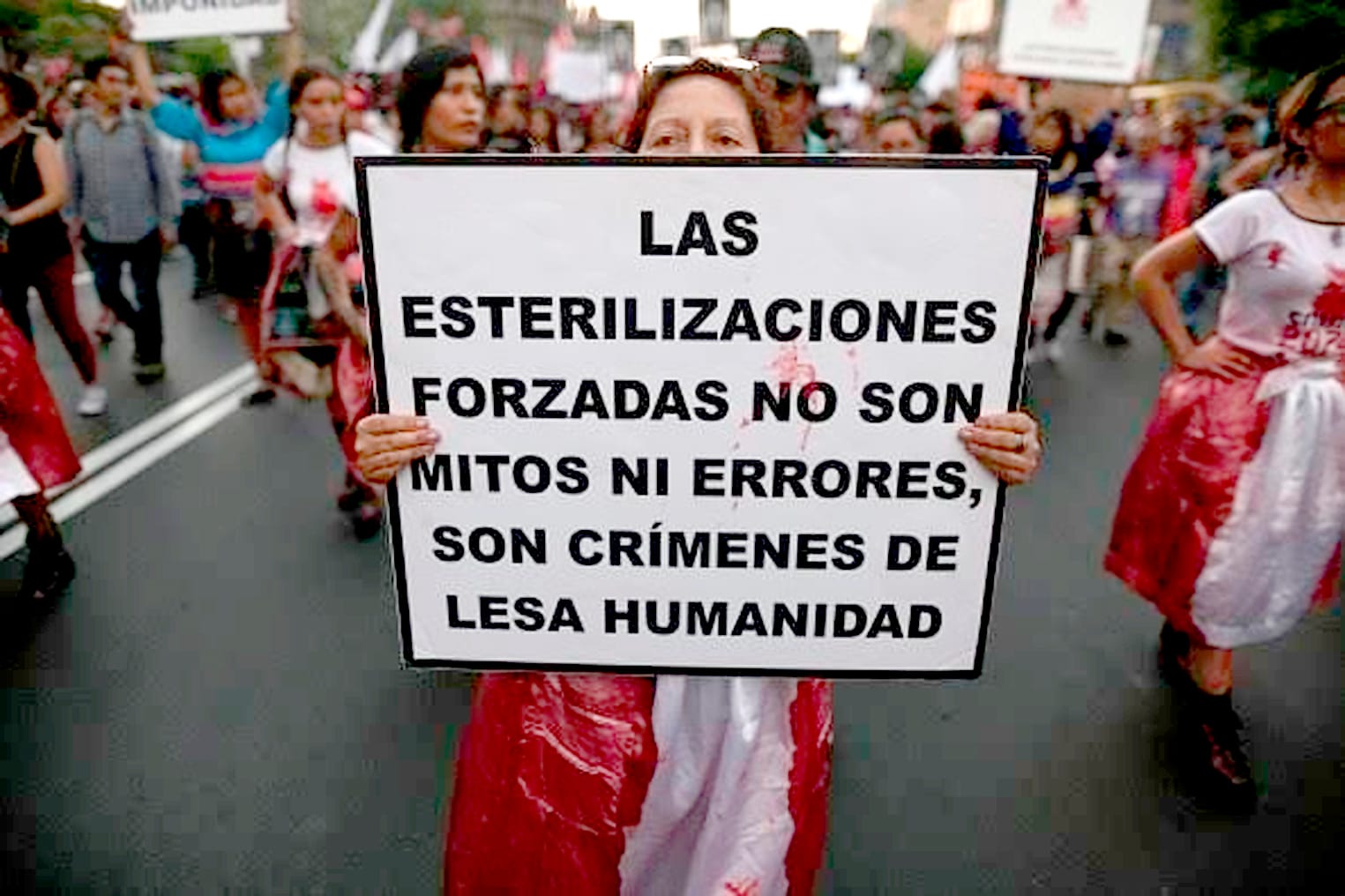 Mulher em protesto segurando um cartaz que lê: 'As esterilizações forçadas não são mitos ou erros, são crimes contra a humanidade'